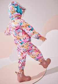 Combinaison colorée et à motifs avec des motifs de dessins animés en rose, bleu et jaune ; dotée d'une capuche et de poignets élastiques, associée à des bottes roses imperméables.