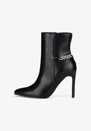 Mustast nahast pahkluu pikkused saapad, millel on terav nina ja kontsas, millel on stiletto-konts. Küljel on dekoratiivne hõbedane kett. Sile tekstuur.