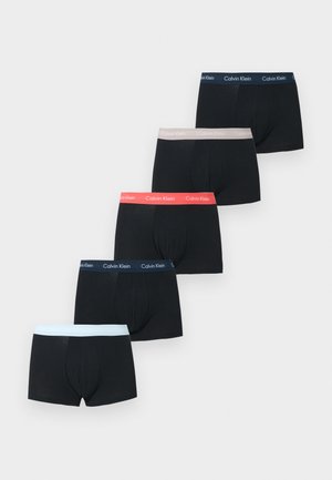 Αθλητικός άνδρας με σκουρόχρωμο δέρμα, όρθιος ξυπόλητος, φορώντας μαύρα εσώρουχα Calvin Klein σε απλό λευκό φόντο.