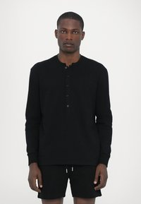 Fekete, hosszú ujjú henley póló puha anyagból, három gombos stash-nyakkal és kerek nyakkivágással, hozzáillő sorttal párosítva.