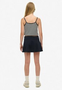 Gestreepte crop top met spaghettibandjes, gecombineerd met een donkerblauwe flared rok. Model draagt witte sokken en lichte schoenen, gezien vanuit de achterkant.