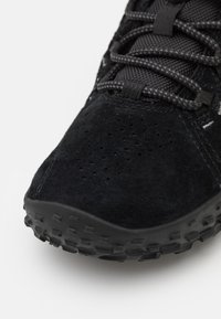 Scarpa sportiva nera con una tomaia in suede, linguetta in mesh testurizzato e suola in gomma con un motivo scolpito. Perforazioni per la traspirabilità.