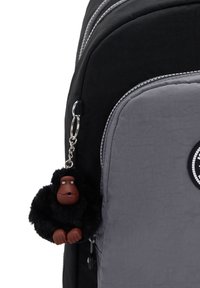 Black and gray backpack with a textured surface, featuring a fur monkey keychain. Accented by silver zippers and a round logo patch.