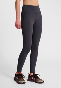 Legginsy treningowe o wysokim stanie, dopasowane do sylwetki, w ciemnoszarym kolorze z gładką fakturą i subtelnym wykończeniem szwów, w połączeniu z wielokolorowym obuwiem sportowym.