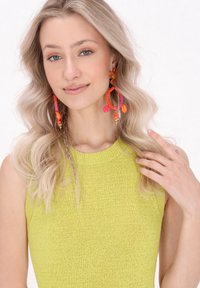 Limegrön ärmlös stickad topp med en texturerad yta, tillsammans med stora, färgglada pärlörhängen i nyanser av rosa och orange.