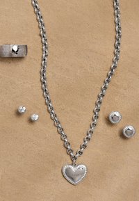 Set di gioielli in argento composto da una collana a catena con pendente a forma di cuore, due orecchini a bottone sferici e un anello decorato.