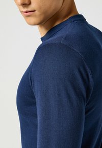 Maglione lavorato a maglia blu navy con scollo rotondo e silhouette aderente, che mette in mostra una texture liscia e dettagli a coste sul colletto e sui polsini.