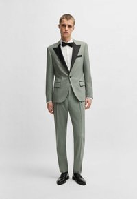 Abito verde chiaro con rever in satin nero, design slim-fit, pantaloni a gamba dritta, tessuto strutturato, abbinato a una camicia bianca e cravatta nera.