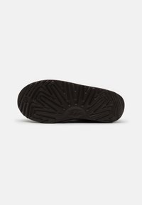 Semelle extérieure en caoutchouc noir avec un motif de crampons en zigzag et le logo UGG. Surface texturée pour une meilleure adhérence, bout arrondi et talon légèrement surélevé.