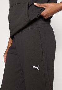 Μαύρο παντελόνι φόρμας από μαλακό ύφασμα, με πλαϊνή τσέπη και λευκό λογότυπο Puma στο αριστερό μηρό. Ελαστική μέση.