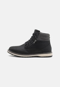 Botas de tobillo negras hechas de material sintético texturizado, con un cierre de cordones en la parte delantera y una cremallera lateral, y una suela de goma blanca en contraste.
