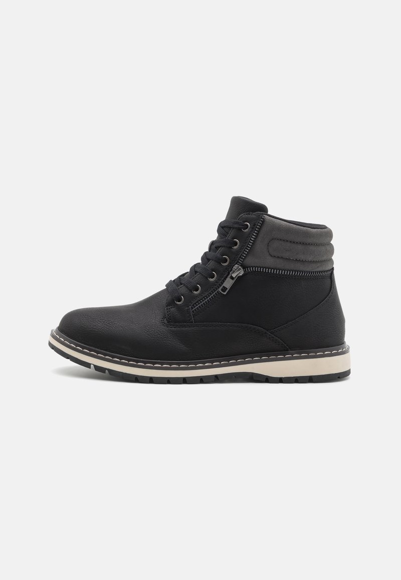 Botas de tobillo negras hechas de material sintético texturizado, con un cierre de cordones en la parte delantera y una cremallera lateral, y una suela de goma blanca en contraste.