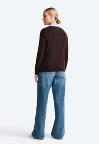 Pull en laine marron avec un col rond, associé à un jean en denim taille haute bleu clair ; texture lisse, coupe décontractée.
