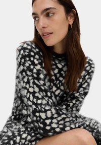 Schwarzer und weißer flauschiger Pullover mit gepunktetem Muster, hohem Hals und langen Ärmeln. Weicher Stoff mit lässiger Passform.