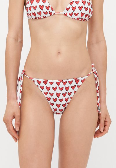 Conjunto de bikini con estampado de corazones rojos sobre fondo blanco. La parte superior tiene copas triangulares, mientras que la parte inferior tiene laterales con lazo y ajuste regulable.