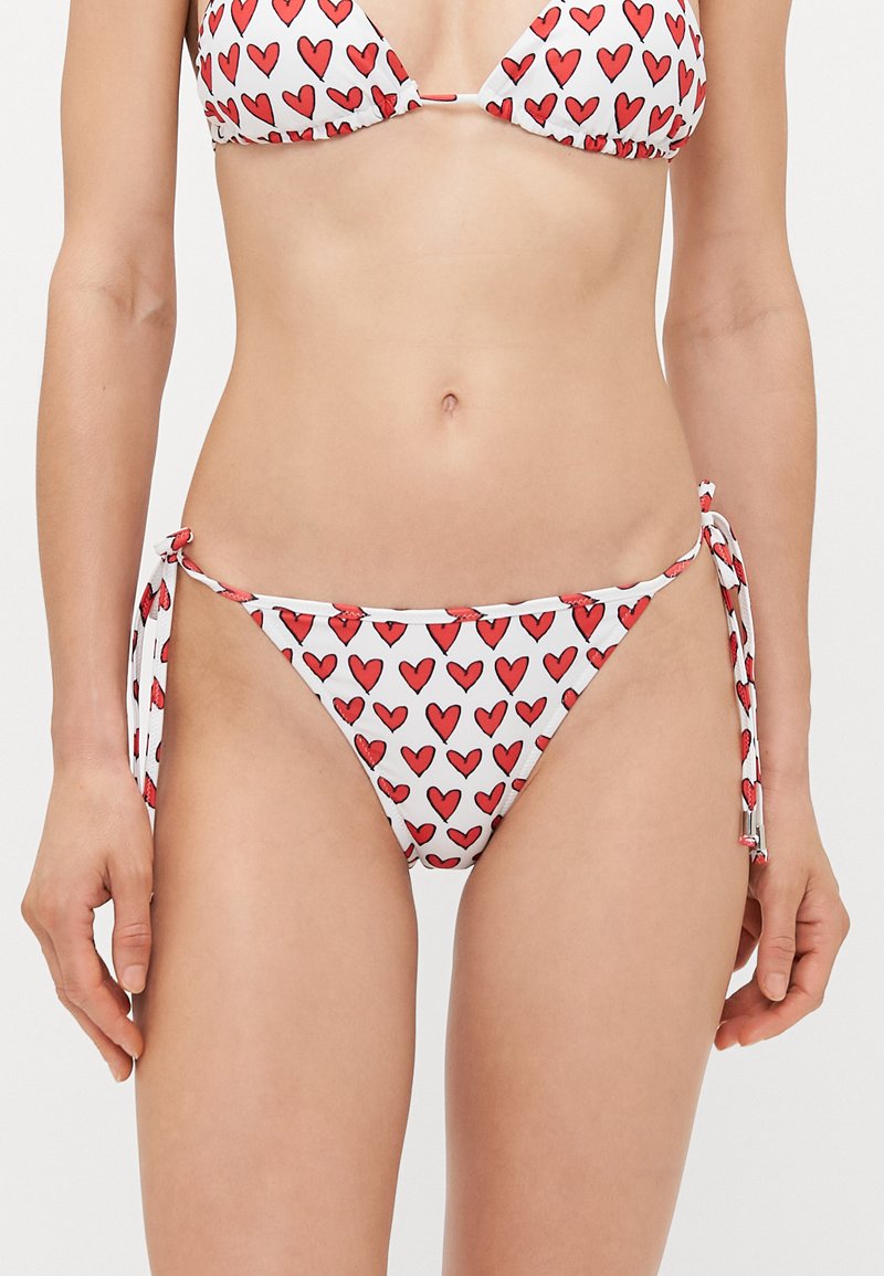 Bikini set featuring red heart print on white fabric. The top has triangular cups, while the bottom has tie sides with adjustable fit.