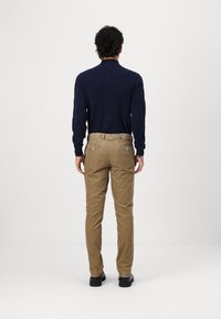 Pull en maille torsadée bleu marine avec col montant, associé à un pantalon en velours côtelé beige. Le pantalon possède des poches arrière et une taille avec passants de ceinture.