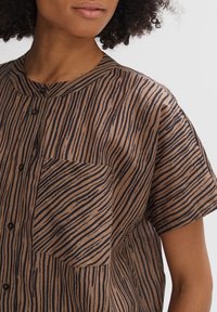 Brown short-sleeve shirt featuring dark wavy stripes, a round neckline, and a chest pocket with a slightly relaxed fit texture.
