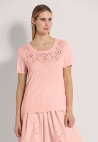 Hellrosa Kurzarm-T-Shirt aus weichem Stoff, mit floralem Ausschnitt-Design entlang des Halsauschnitts und einem lässigen Schnitt.