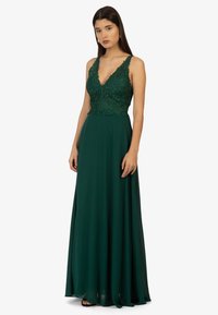 Grünes Abendkleid mit tiefem V-Ausschnitt und besticktem Oberteil. Fließender, bodenlanger Rock aus leichtem Stoff.