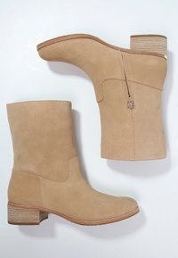 Bottines beige en daim avec une finition lisse, un petit talon empilé et une fermeture éclair sur le côté pour un enfilage facile.