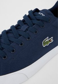 Zapatilla de lona marina con punta redonda, suela de goma blanca y cierre con cordones. Presenta un logo de reptil bordado en el lado.