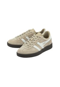 Beige suède sneakers met witte diagonale strepen en logo, voorzien van een ronde neus, vetersluiting en een donkere rubberen zool.