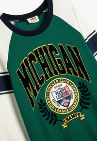 Camiseta de raglán verde y blanca con acentos en azul marino. Presenta "MICHIGAN" en texto amarillo en negrita y un gráfico circular con hojas de laurel.