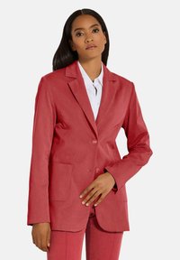 Roter Blazer aus strukturiertem Stoff, mit einer Zwei-Knopf-Front, Reverskragen und zwei vorderen Taschen, getragen über einem weißen Hemd.