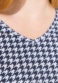 Stoff in Marineblau und Weiß mit einem Hahnentritt-Muster und dezentem Glanz, V-Ausschnitt-Design und einer weichen Textur.