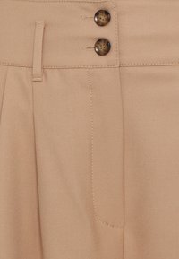 Beige pleated trousers with a smooth texture, featuring two brown buttons at the waist and a side pocket with neat stitching details.