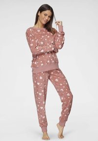 Pink fleece pajama set featuring scattered white heart patterns, long sleeves, ribbed cuffs, and a relaxed fit for comfort.