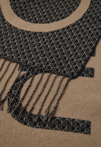 Vevet tørklæde i beige og mørkeblå, med et geometrisk mønster og frynse detaljer. Blød tekstur med kontrasterende farveakcenter.