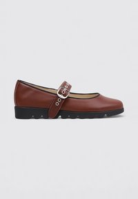 Zapatos Mary Jane de cuero marrón con punta redondeada, correa ajustable con hebilla de plata y suela de goma negra texturizada.