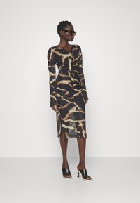 Robe longue à manches longues noire et beige avec une silhouette ajustée, texture froncée et imprimé abstrait. Présente une fente sur le côté et est assortie à des mules noires.