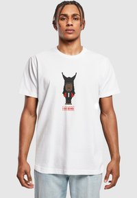 Hvid bomulds t-shirt med en tegneseriefigur, der har en sort beanie og røde detaljer. Teksten nedenfor siger "JEG ER MUSIK" med fede røde bogstaver.