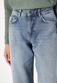 Ljusblå denimjeans med rak ben, framfickor och hög midja, med kontrasterande sömmar och klinkknappslås.