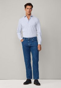 Lichtblauw gestreept overhemd met knopen, gecombineerd met donkerblauwe jeans en zwarte schoenen. Het overhemd heeft een klassieke kraag en een getailleerd ontwerp.