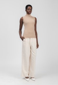 Top in maglia senza maniche color beige con collo alto abbinato a pantaloni larghi color crema chiaro e tacchi a punta bianchi. Tessuto morbido, vestibilità comoda.