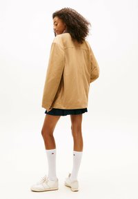 Beżowa, oversize kurtka o gładkiej fakturze, z detalem szwu z tyłu. Noszona z ciemną spódnicą i białymi skarpetkami do kolan. Białe sneakersy.