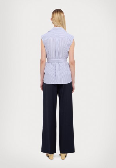 Mouwloze, gekraagde top met blauw-witte verticale strepen, ceintuur in de taille, gecombineerd met wijde, donkere pants. Soepele stoftextuur.