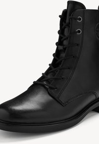 Bottine en cuir noir avec lacets à l'avant, bout arrondi et petit talon, présentant des coutures détaillées sur une surface supérieure lisse.