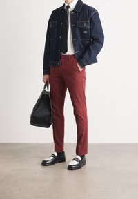 Kurtka dżinsowa z dwoma kieszeniami na piersi, biała koszula, czarny krawat, czerwone spodnie, czarna torebka oraz czarne mokasyny z białymi detalami.