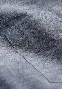 Gros plan sur un tissu gris à texture fine tissée, présentant des motifs géométriques et floraux subtils dans une teinte légèrement plus foncée.