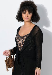 Svart stickad cardigan med strukturerad yta, lager-på-lager över en leopardmönstrad topp med spetsdetalj; ihop med en liten, intrikat detaljerad brun väska.