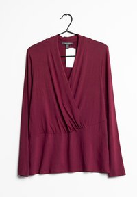 Bordowy top z długim rękawem o kroju typu wrap, z dekoltem w kształcie litery V i marszczonym wcięciem w talii. Wykonany z miękkiego, elastycznego materiału, wisi na czarnym wieszaku.