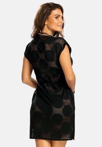 Czarna sukienka z siateczki z dużymi okrągłymi wzorami, krótkimi rękawami, paskiem w talii i okrągłym dekoltem. Teksturowana z użyciem przewiewnej tkaniny.
