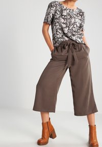 Haut à manches courtes imprimé animalier en nuances de beige et noir, associé à un pantalon large taille haute marron et des bottines à talons marron.