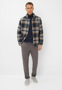 Ruitjes flanellen overhemd in marine, grijs en bruin; marine coltrui; grijze broek; grijze sneakers met witte zolen; casual pasvorm.