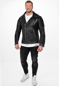 Zwart leren motorjack met geribbelde schouderdetails, ritsen aan de voorkant en een slim fit. Draag dit met versleten donkere jeans en witte sneakers.